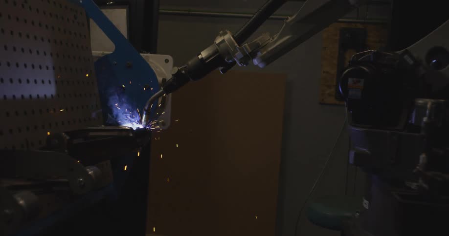 A robotic arm performs welding in a dark industrial setting