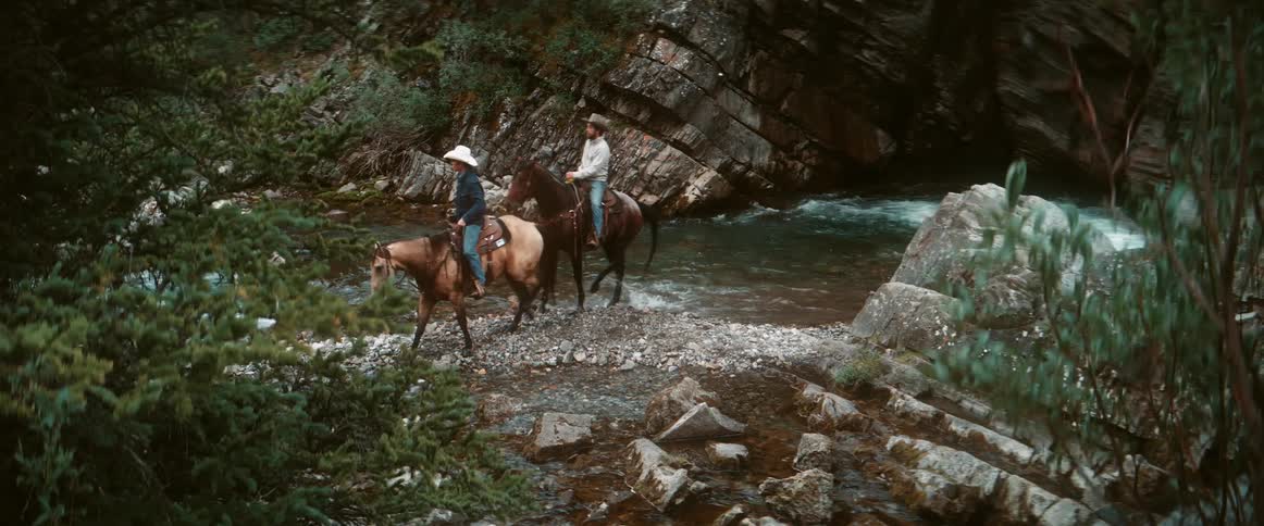 Two men ride their horses in the stream water
