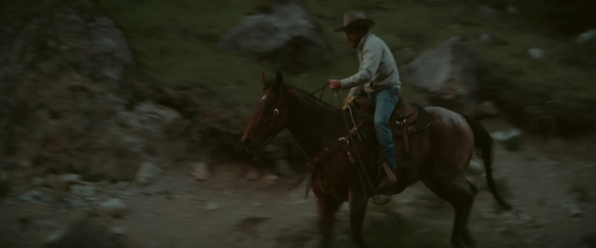 Two people in hats riding horses through the mountains