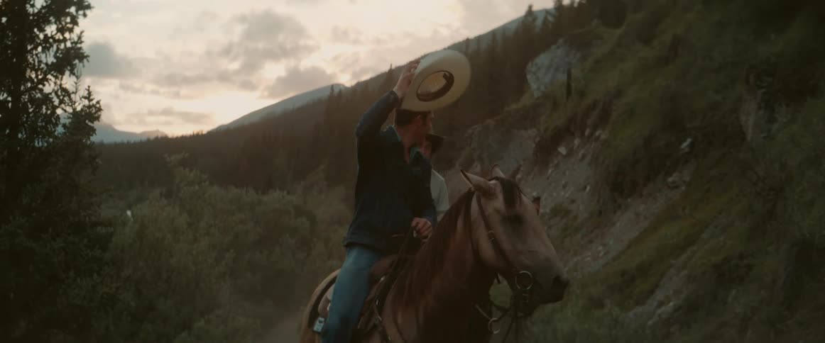 Two men ride on horses through a mountain path in the wilderness