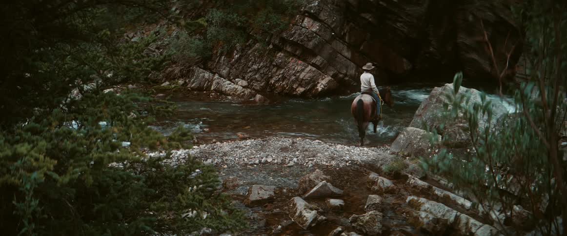 A person rides a horse back and forth into and out of a stream