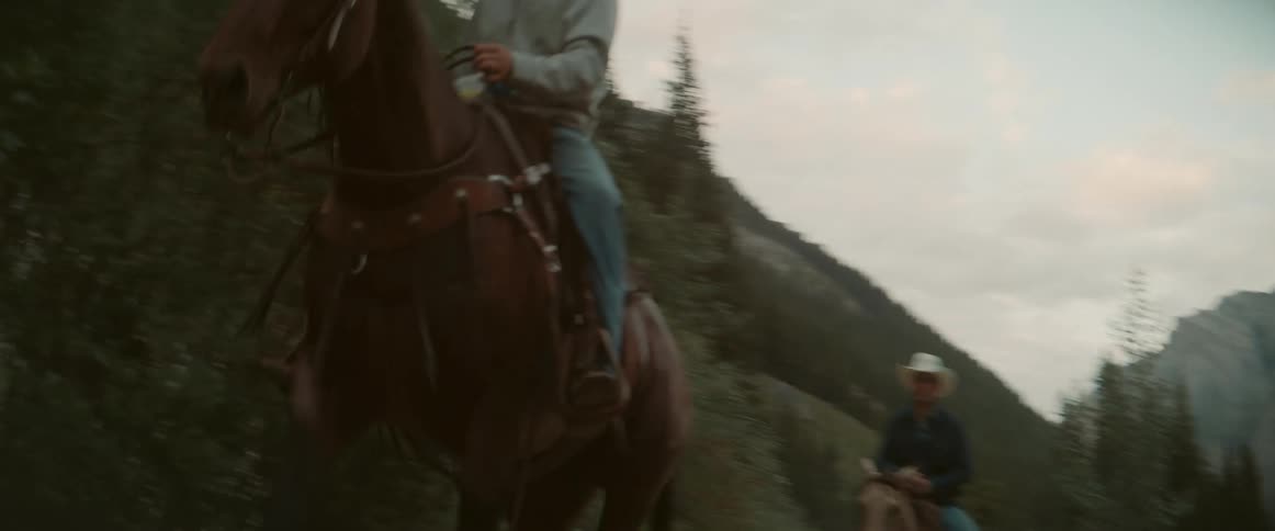 Two cowboys ride their horses past the mountain