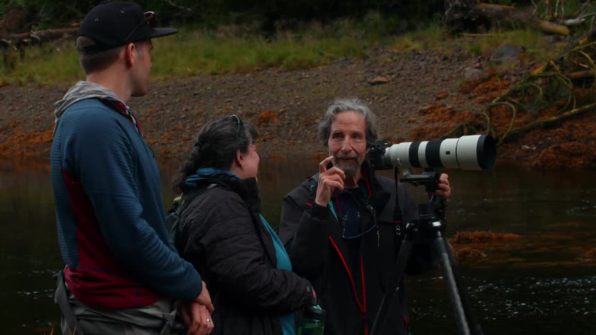 A man with a camera is talking and laughing by the water