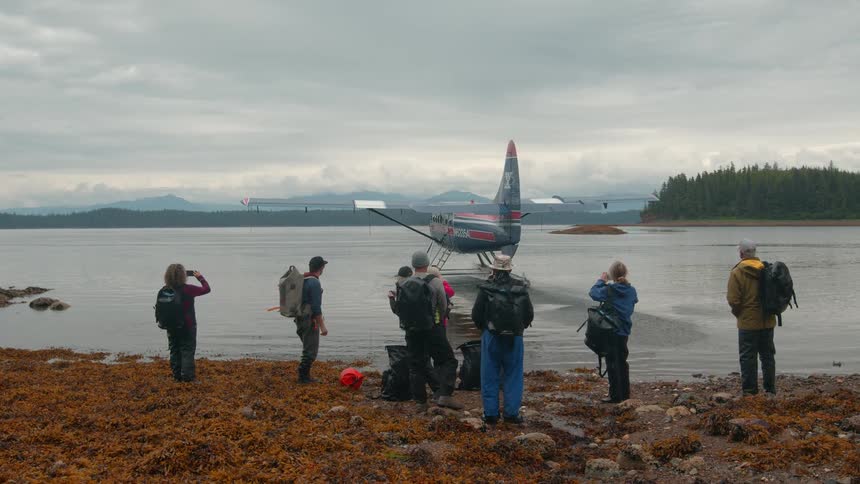 Group of travelers with backpacks watching a water plane take off