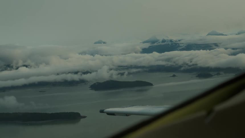 Aerial view of misty islands and snow capped mountains seen from an airplane window