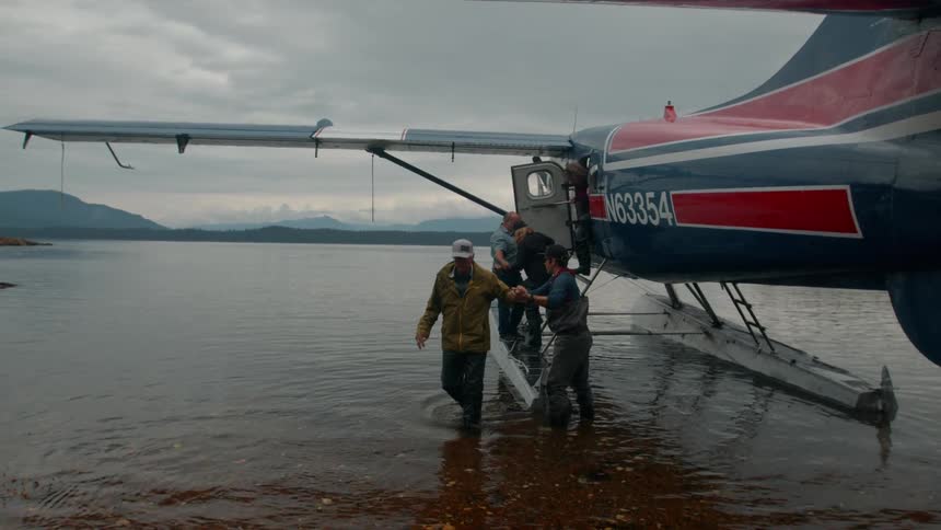 On a cloudy day a group of people are helped down from a seaplane into the water the first person walks to shore while the others continue to make their way down