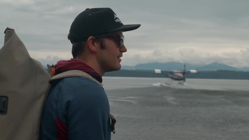 Man wearing glasses and a cap watching a water plane take off
