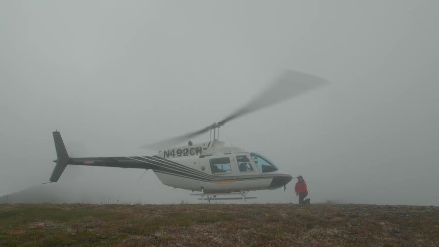 Person in red jacket on a mountain facing a helicopter with its blades on