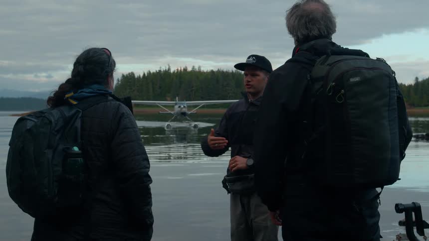 A man is taking with two hikers by the plane on the water