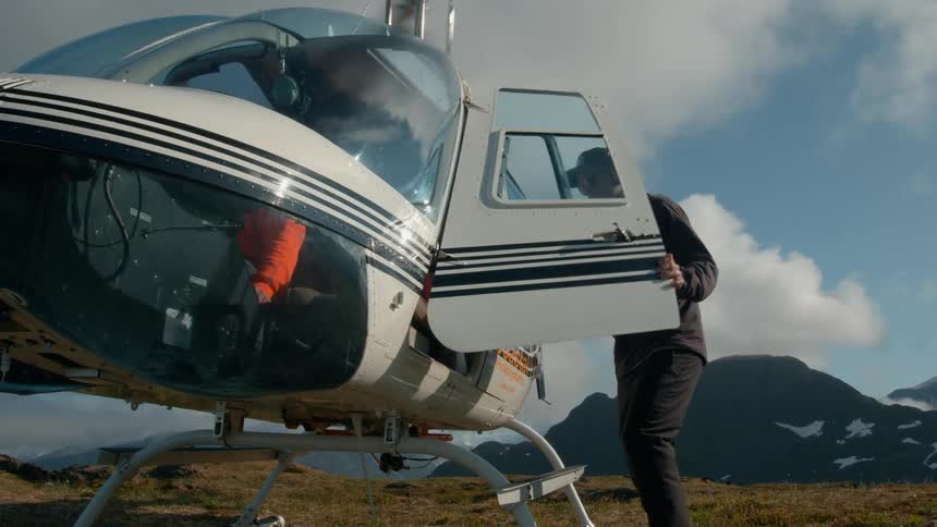Man prepares to enter a helicopter in a remote mountain area