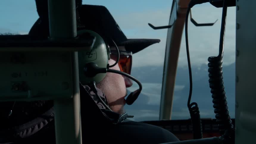 Man with headset inside a helicopter flying over a mountainous area