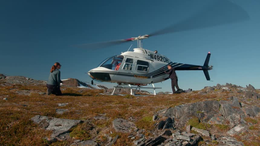 Woman crouches as man removes suitcases from helicopter on mountain