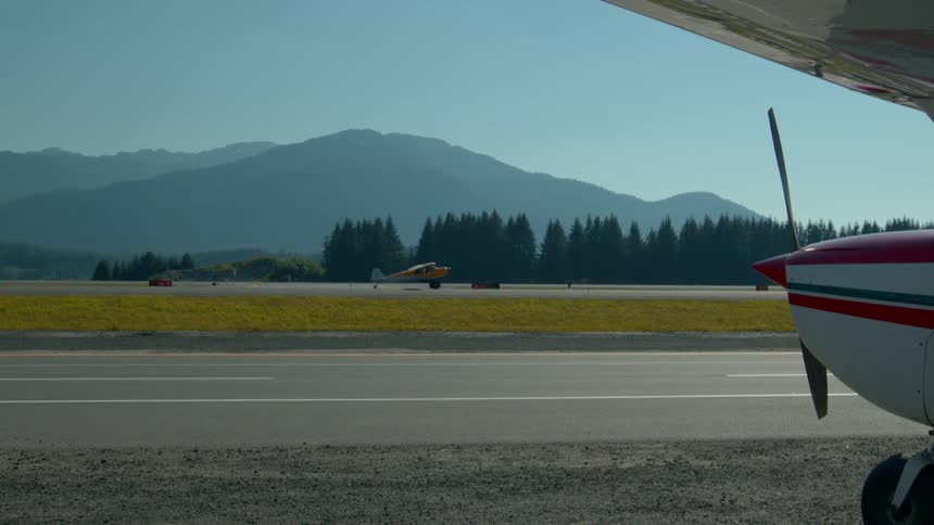 An aircraft takes off from the runway while another plane is parked on the side at midday