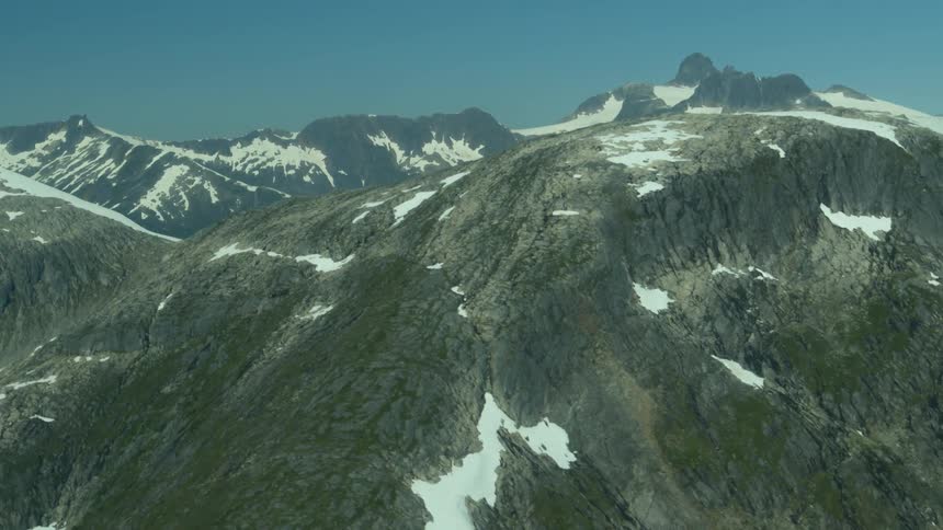 A high mountain is partially covered in snow at midday