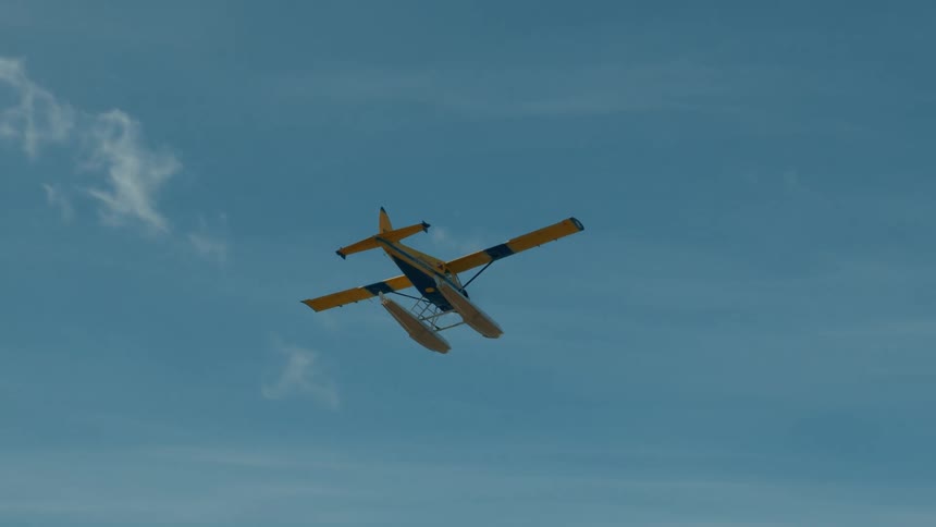 A small airplane flies over a forested mountain landscape under cloudy skies