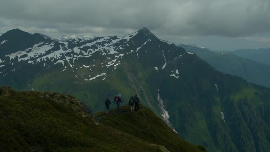 Four people hike at the top of a mountain wearing winter clothing on a cloudy day