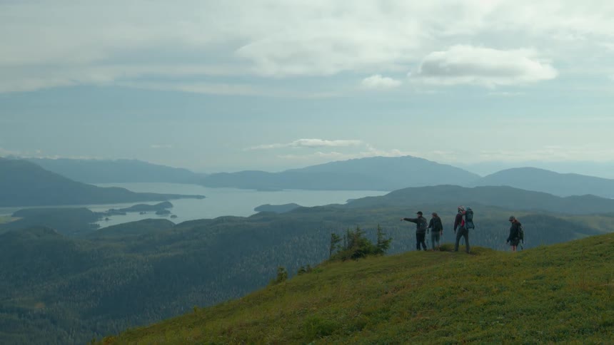 Group of people hiking up a green mountain on a partly cloudy day