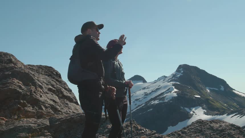 Two hikers stand on a rocky peak admiring the snowcovered mountain landscape