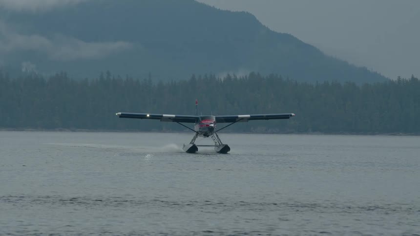 Seaplane approaches to land on a calm lake surrounded by misty forested mountains