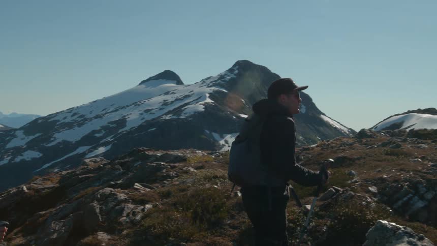 Two hikers walk across rocky alpine slopes beneath snow capped peaks