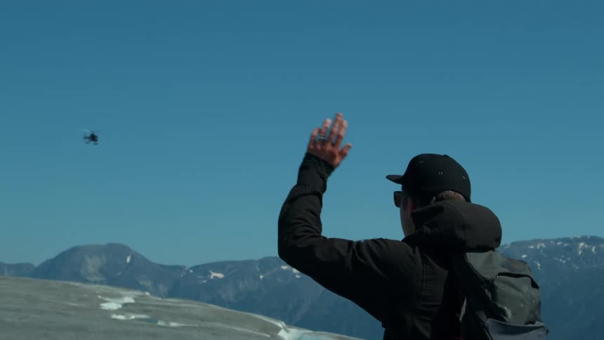 Person in cap and backpack on a mountain waving to a helicopter