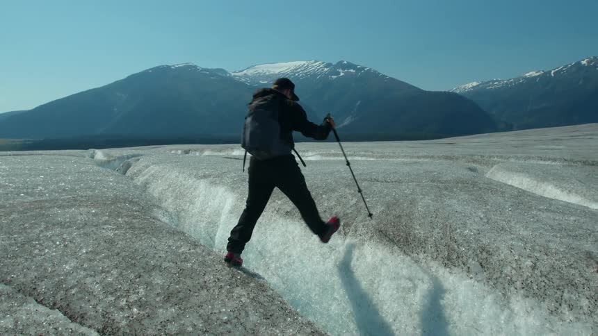 A hiker carefully walks across a glacier using a trekking pole