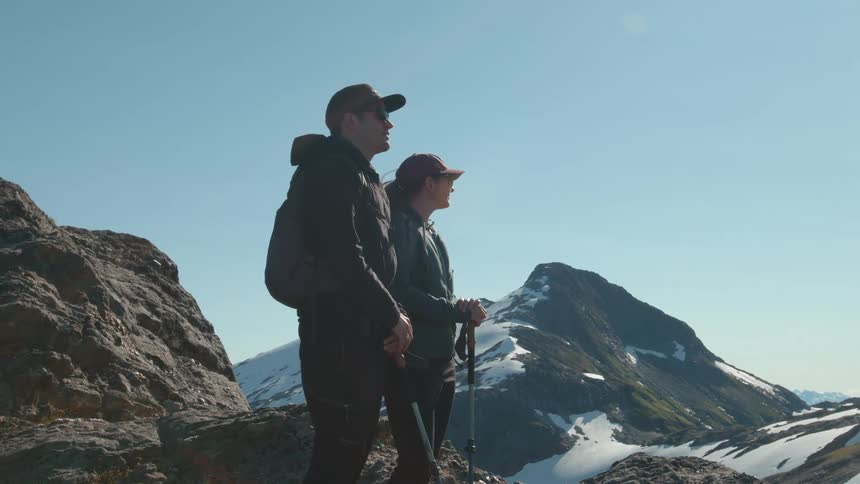 Two hikers standing on a rocky mountain peak gazing out at the snow covered landscape