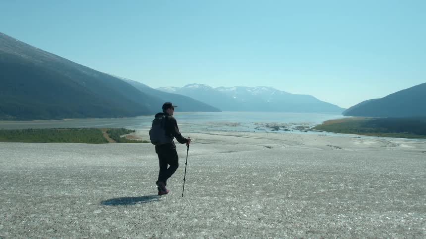 A lone hiker crosses a vast icy plain surrounded by mountains under a clear sky