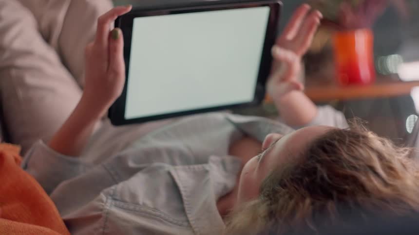 Woman lying on a sofa interacting with a tablet