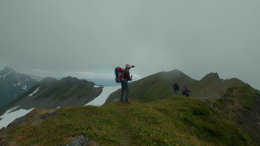 Hikers trek along a mountain ridge under overcast skies