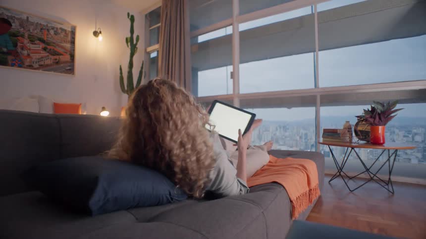 Woman relaxes on a couch using a tablet in a high rise apartment
