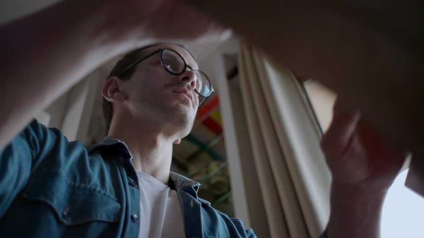 A lowangle shot of a man wearing glasses and a denim shirt looking intently downwards he appears to be opening or looking into a box or container with the edges of it visible in the foreground