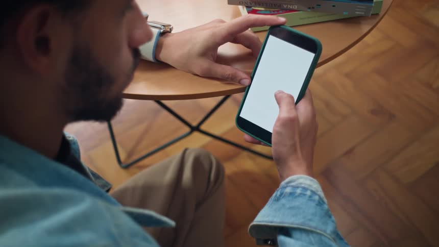 A man interacts with a smartphone while seated at a small indoor table