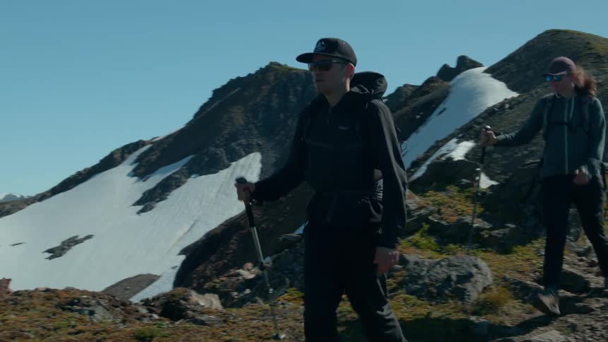Two hikers trek along a rugged mountain trail in bright daylight