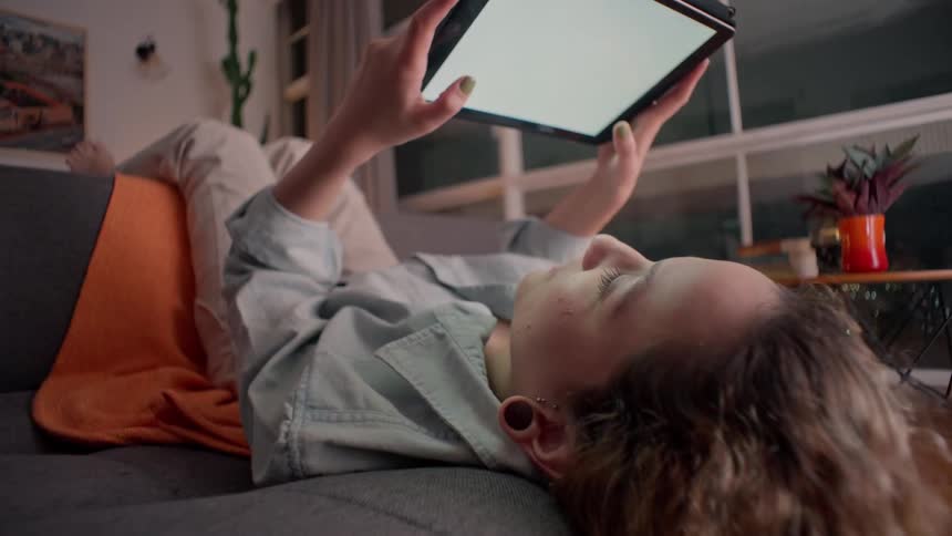 Woman lying on a couch holding a tablet above their face
