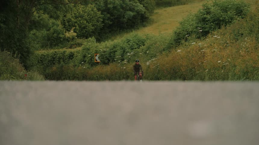 Person riding a bicycle in an asphalted environment surrounded by nature