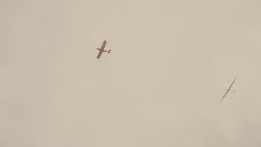 Engine plane and glider cross the beige sky covered with thin clouds