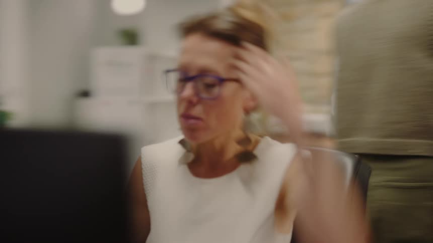 Slow shutter blurred shot of a woman wiping her forehead as she quickly types on her computer keyboard