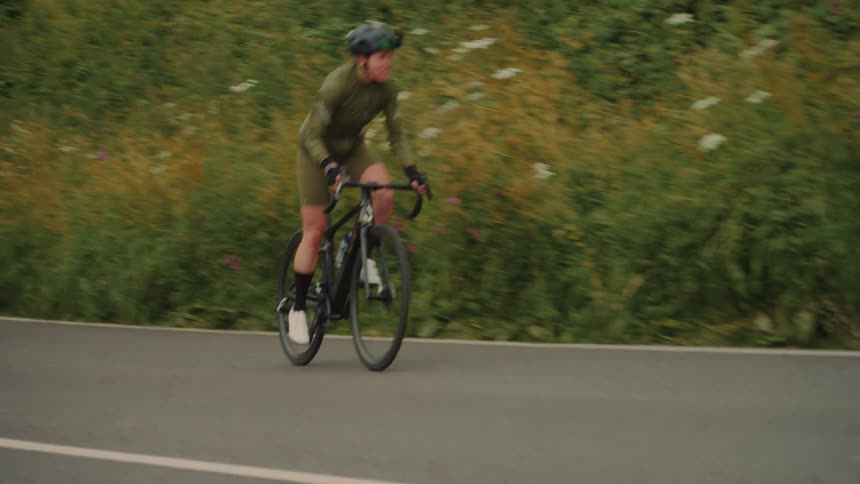 A man rides his bike uphill along a road bordered by thick grass