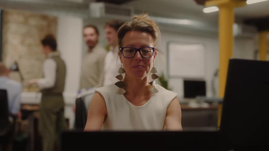 Woman with large glasses and flashy earrings works focused in a modern office