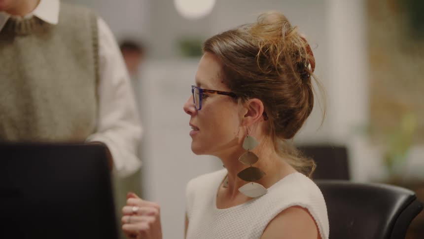 Blonde woman sitting in a work environment talking to another person