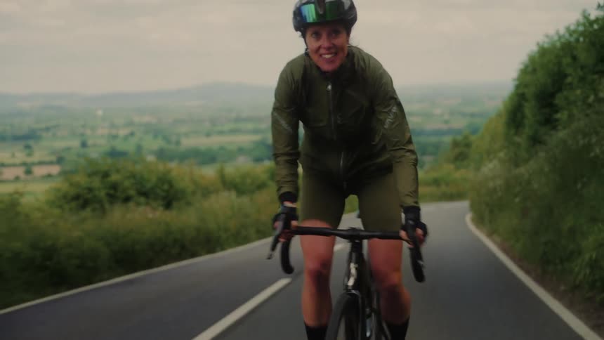 A woman smiles as she pedals her bike uphill on a paved road