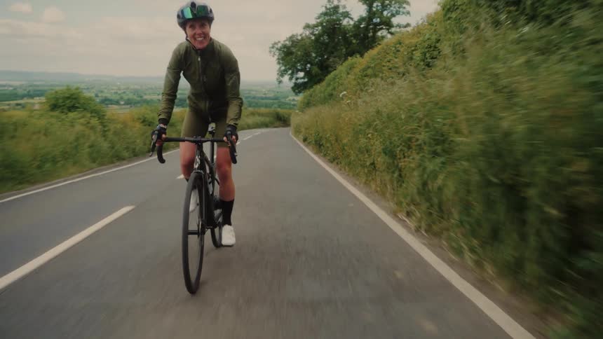 Cyclist rides along a narrow country road surrounded by greenery