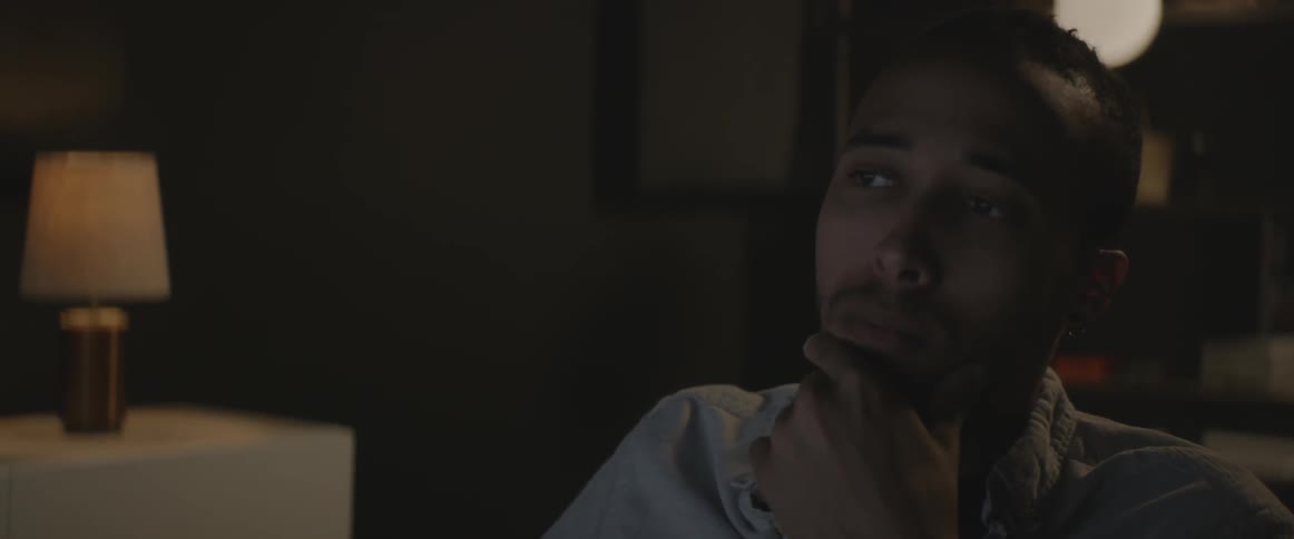 A man sits in a dark room rubbing his chin