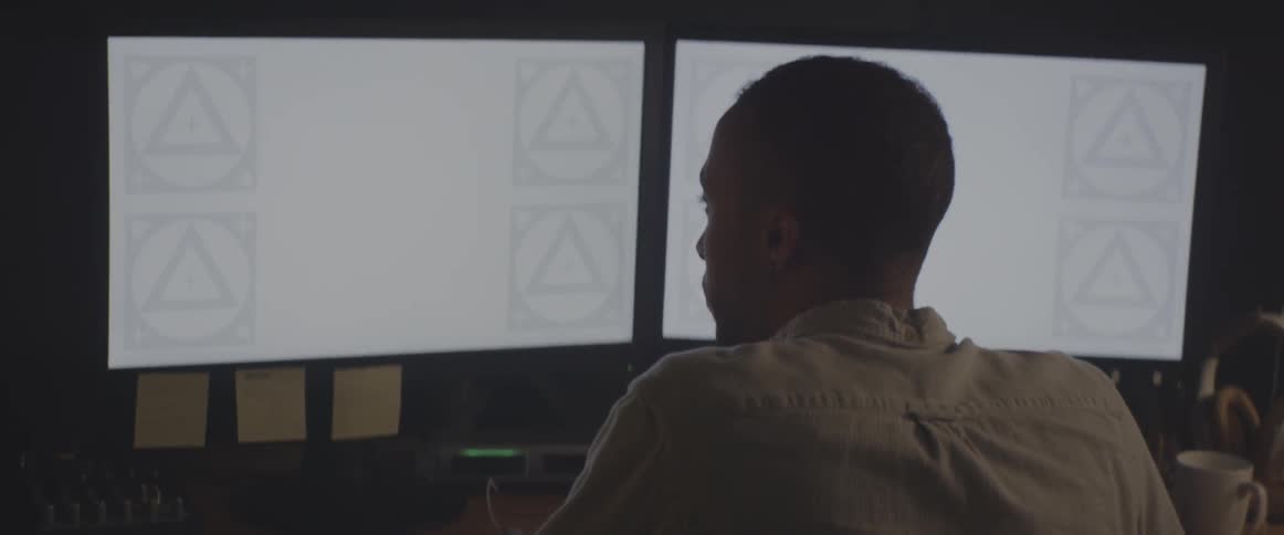A man sits working at a desk with two computer monitors