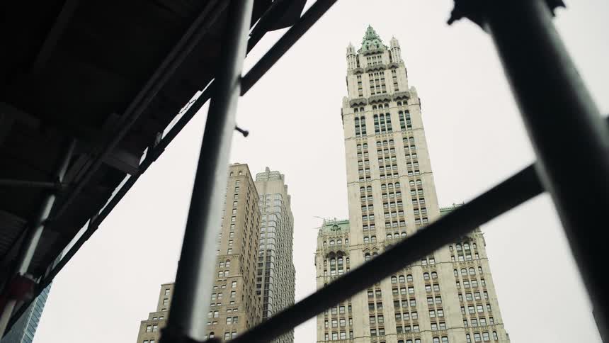 Tall buildings with classical architecture appear behind metal scaffolding seen from below
