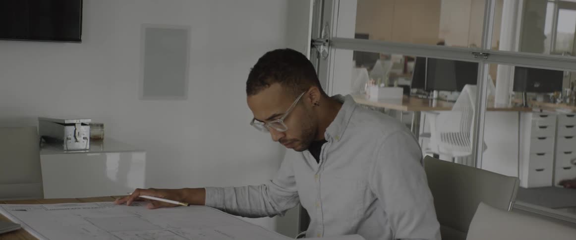 A man sits at a desk and flips through blueprints