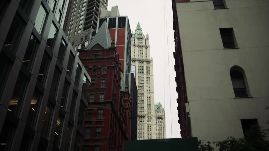 A cityscape featuring a mix of tall buildings including a white spired tower red brick structure with a gabled roof and modern glassfronted facades under clear daylight
