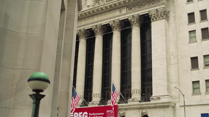 The new york stock exchange nyse building in the financial district of lower manhattan displays three american flags hanging in front at midday