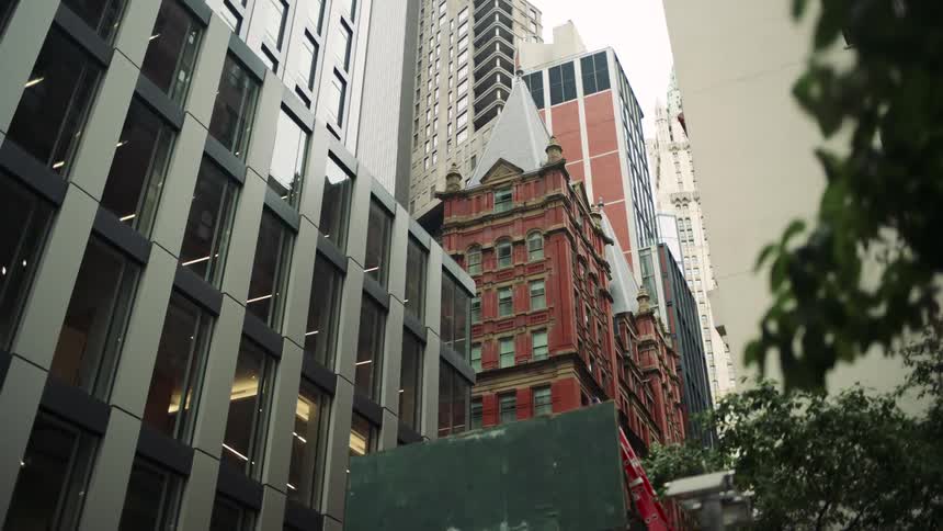 Cinematic view of tall buildings starts with some tree leaves and after that reveals big buildings